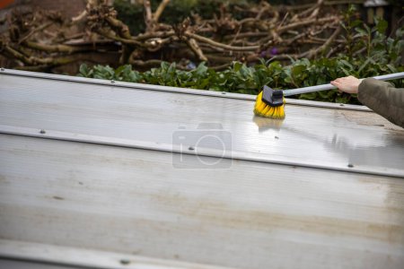 Photo for Washing the patio pergola roof cover made of aluminum. removing the dirty algae with brush soap and water close up in garden from a house terrace cleaning, workers, concept - Royalty Free Image