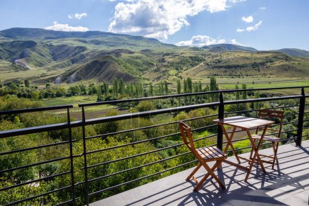 Photo for Table with two chairs on a wooden terrace in Aspindza town, Georgia, with Mtkvari river valley landscape view in Samtskhe - Javakheti region, Lesser Caucasus mountains. - Royalty Free Image