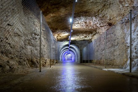 Téléchargez les photos : Tunnel en pierre percé sous terre dans la roche avec des illuminations bleues et une clôture de protection, sortie du monument naturel de la grotte Prometheus en Géorgie. - en image libre de droit