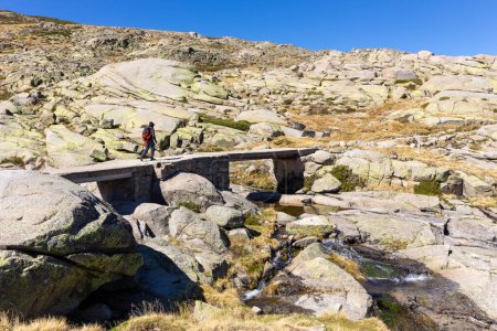 Photo for Male tourist hiking on stone bridge, trail to the Laguna Grande de Gredos lake from the Plataforma de Gredos in Sierra de Gredos mountains, Spain. - Royalty Free Image