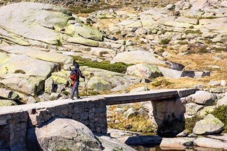 Photo for Male tourist hiking on stone bridge, trail to the Laguna Grande de Gredos lake from the Plataforma de Gredos in Sierra de Gredos mountains, Spain. - Royalty Free Image