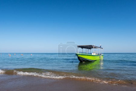 Petit bateau vert en bois ancré sur la plage avec des vagues écrasant le rivage, Fujairah, Émirats arabes unis.
