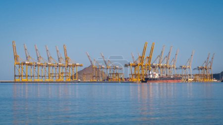 Grues portuaires chargeant des porte-conteneurs dans le port de Fujairah, Émirats arabes unis. Lignes de grues portuaires jaunes contre la mer bleue et le ciel.