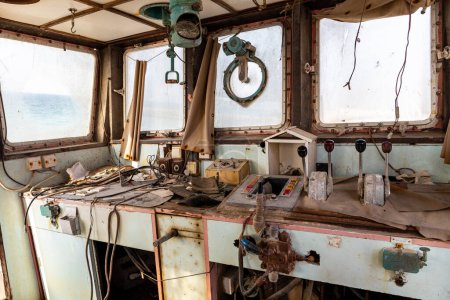 Abandoned and demolished cargo ship bridge inside view with throttle levers, communication devices and equipment, shipwreck beached on the Al Hamriyah beach in Umm Al Quwain, United Arab Emirates.