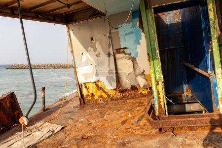 Desolada y oxidada cubierta de un buque de carga con viejo puente encallado en la playa de Al Hamriyah en Umm Al Quwain, Emiratos Árabes Unidos, vista al mar y rompeolas en el fondo.