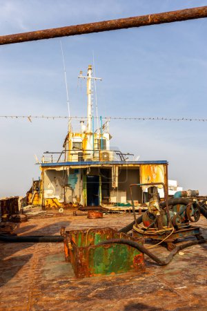 Demolished and rusty deck of a cargo ship with old bridge, mast, antennas and machinery, washed ashore on the Al Hamriyah beach in Umm Al Quwain, United Arab Emirates.