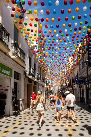 Photo for RONDA, Spain, 02.09.19. Calle La Ronda picturesque narrow street with colorful balls decorations hanging, bars, shops, restaurants and cafes, many tourists walking on sunny summer day. - Royalty Free Image