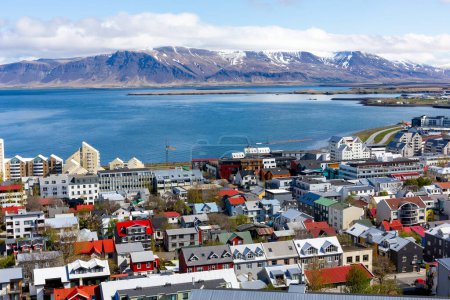 Téléchargez les photos : Reykjavik, Islande, vue sur le paysage de la ville avec des bâtiments résidentiels colorés, vue sur l'océan et la chaîne de montagnes enneigée du mont Esjan en arrière-plan vu du clocher de l'église Hallgrimskirkja. - en image libre de droit