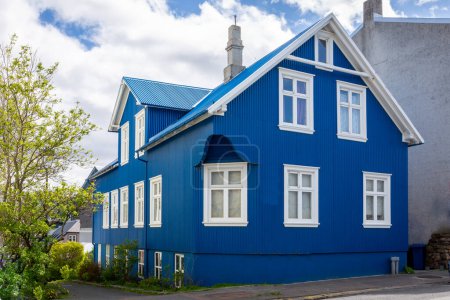 Traditional Icelandic blue residential house with gable roof, white window frames, clad in corrugated metal sheets in Reykjavik, Iceland.