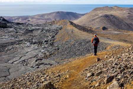 Männliche Touristen beim Wandern am Lavafeld des Vulkans Fagradalsfjall, gefrorene basaltische Lavalandschaft nach einem Ausbruch, Island.