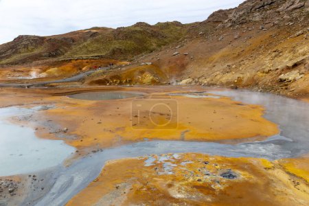 Paisaje del área geotérmica de Seltun en Krysuvik con aguas termales a fuego lento, colores amarillo y naranja de colinas de azufre y sendero turístico, Islandia.