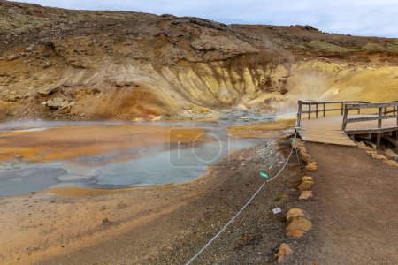 Landschaft des Seltun Geothermalbereichs in Krysuvik mit simmernden heißen Quellen, gelben und orangen Schwefelfarben und Touristenpromenaden, Island.