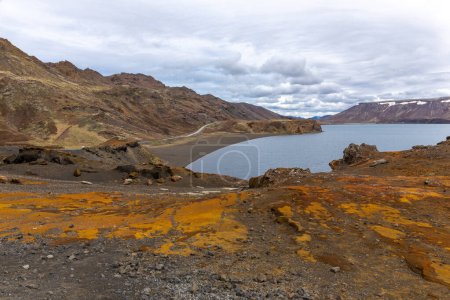 Landschaft der Halbinsel Reykjanes mit dem Kleifarvatn-See, kargen Lavafeldern, die mit Moos bedeckt sind, orangefarbenem Schwefelboden und kurvenreicher Straße entlang der Küste.