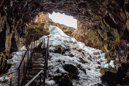 Der Lavatunnel (Raufarholshellir) in Island, Innenansicht des Eingangs zur Lavaröhre mit eingestürzter Decke, Metallsteg und Schnee.