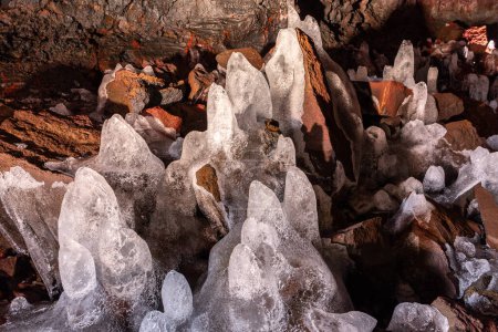 Estalagmitas de hielo (carámbanos) formadas en la superficie de roca volcánica de hierro rojo en el túnel de lava (Raufarholshellir) en Islandia.