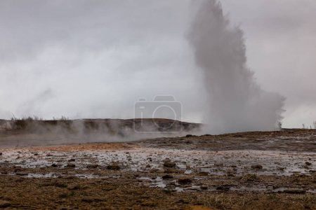 Strokkur geyser erupting, fountain-type geyser in geothermal area in Iceland, people watching in the background.