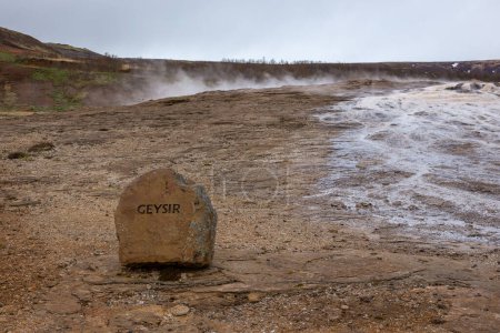 El Gran Geysir en la zona geotérmica de Islandia, humeante piscina de aguas termales géiser con letrero de información de piedra "Geysir".