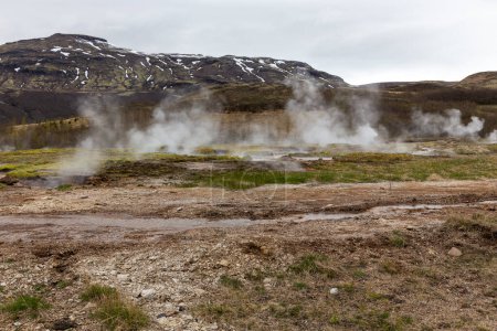 Foto de Geysir área geotérmica en el valle Haukadular, Islandia, con aguas termales humeantes, arroyos de agua caliente y montañas en el fondo, sin personas. - Imagen libre de derechos