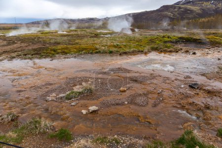 Geysir geothermal area in Haukadular valley, Iceland, with steaming hot springs, hot water streams and brown sulfurous water, no people.