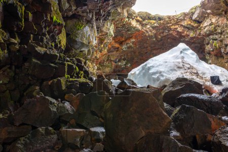 El túnel de lava (Raufarholshellir) en Islandia, vista interior de la entrada al tubo de lava con techo colapsado, piedras y nieve.