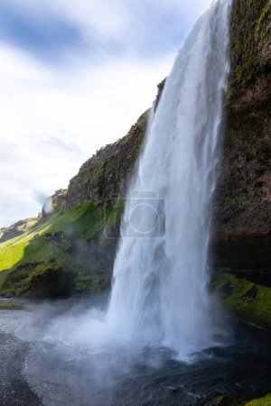 Seljalandsfoss, a walk-behind waterfall in South Iceland, with tumbling water and spray, tourist footpath and cavern behind the waterfall, spring view, no people.