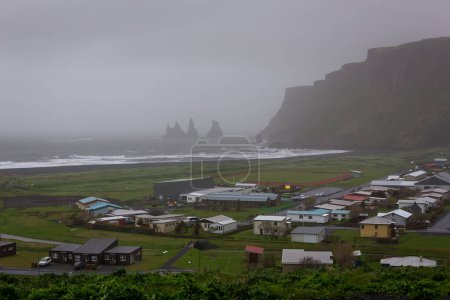 Foggy paysage de Vik i Mydral littoral en Islande avec Reynisfjara Black Sand Beach, empilements de mer de basalte Reynisdrangar et falaises verticales.