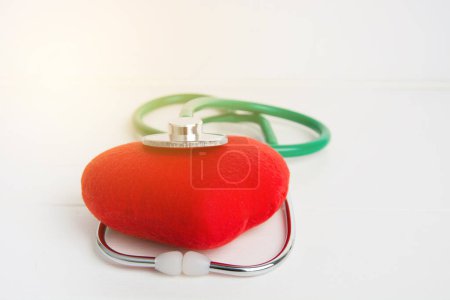Photo for Green stethoscope and red heart isolated with sunshine on wooden white background - Royalty Free Image