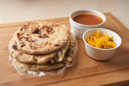 Photo for Central America traditional pupusas, a flavorful delight from El Salvador, Honduras, and Nicaragua, served with curtido and sauce on a rustic wooden tray - Royalty Free Image