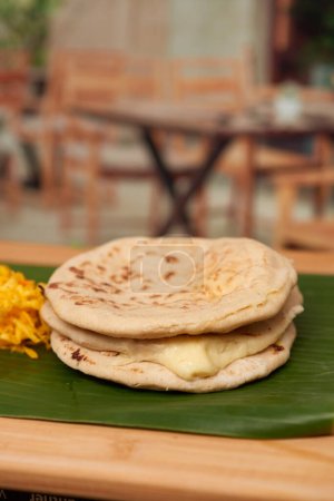 Photo for A captivating photo of authentic Salvadoran pupusas, featuring a cheesy filling and culinary artistry, set in a restaurant-style ambiance on a wooden surface accentuated by a leaf - Royalty Free Image
