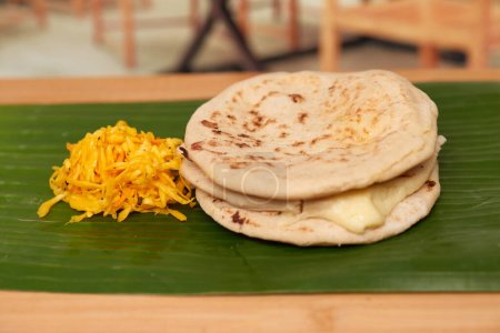 Photo for A captivating photo of authentic Salvadoran pupusas, featuring a cheesy filling and culinary artistry, set in a restaurant-style ambiance on a wooden surface accentuated by a leaf - Royalty Free Image
