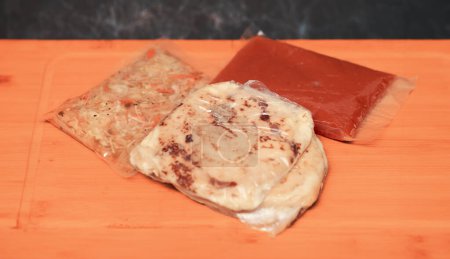 pupusas ake-away enveloppés dans du papier et du plastique, servis avec du curtido et de la sauce, prêts à déguster n'importe où.
