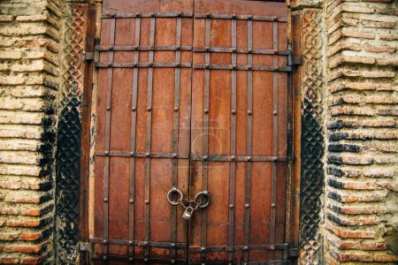 Close up of a heavy wooden plant double door, with iron hinges and handles,closing off the entrance into an old brick building. High quality photo