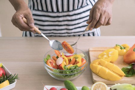 Téléchargez les photos : The concept of a healthy diet and lifestyle. Man is preparing a salad of various vegetables in the kitchen. - en image libre de droit