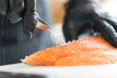 Foto de Chef preparing a fresh salmon fillet in Japanese kitchen. Close up hand of chef Pulling salmon fish bone for making sashimi. - Imagen libre de derechos