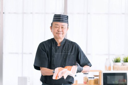 Téléchargez les photos : Portrait de chef joyeux debout avec des poissons de saumon. Chef coupant du poisson et faisant du sashimi. - en image libre de droit