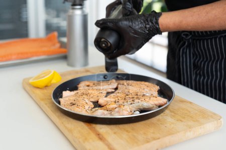 Photo for Chef preparing a fresh salmon. Japanese Chef sprinkle black pepper on salmon meat. - Royalty Free Image
