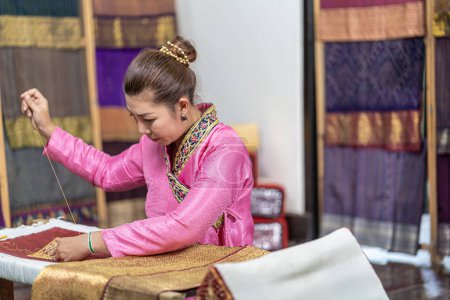 Photo for Crafts and craftsmanship.  Asian woman embroidering golden thread on silk. Yong woman are Sewing silk. - Royalty Free Image