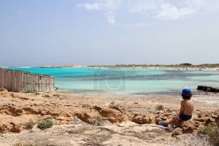 Téléchargez les photos : Petit enfant assis près de la plage de Ses Illetes, l'un des endroits les plus étonnants et emblématiques de l'île de Formentera, Espagne. - en image libre de droit