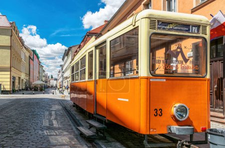 Bydgoszcz, Poland - June 13, 2023: Vintage yellow tram on the street in the historical district of Bydgoszcz. Sunny cityscape and beautiful sidewalk cafe