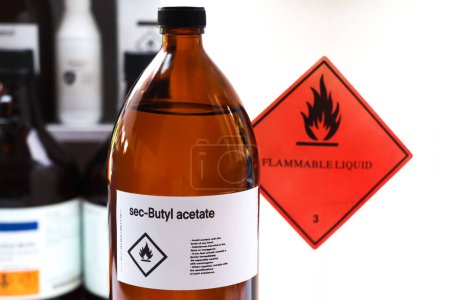 Foto de Acetato de sec-butilo en vidrio, productos químicos peligrosos y símbolos inflamables en recipientes de la industria o el laboratorio - Imagen libre de derechos