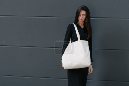 Téléchargez les photos : Femme tenant sac éco textile blanc sur fond urbain. Concept d'écologie ou de protection de l'environnement. Sac écologique blanc pour maquettes
. - en image libre de droit