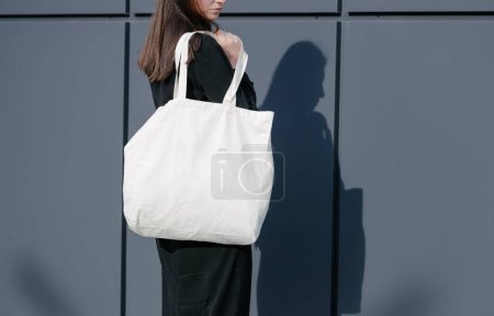 Photo for Woman holding white textile eco bag against urban city background. Ecology or environment protection concept. White eco bag for mock up. - Royalty Free Image