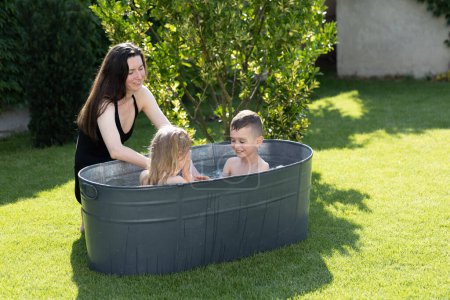 Photo for Mother having fun with children in an outdoor bath tube in the backyard in summertime - Royalty Free Image