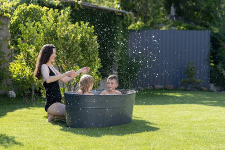 Téléchargez les photos : Mère s'amuse avec des enfants dans une baignoire extérieure dans la cour en été - en image libre de droit