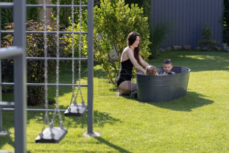 Foto de Madre divirtiéndose con los niños en un tubo de baño al aire libre en el patio trasero en verano - Imagen libre de derechos