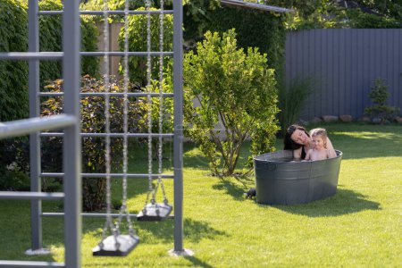 Téléchargez les photos : Mère s'amuse avec un enfant dans une baignoire extérieure dans la cour en été - en image libre de droit
