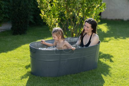 Foto de Madre divirtiéndose con un niño en un tubo de baño al aire libre en el patio trasero en verano - Imagen libre de derechos