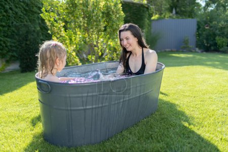 Photo for Mother having fun with a child in an outdoor bath tube in the backyard in summertime - Royalty Free Image