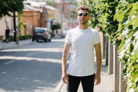 Téléchargez les photos : Hipster beau modèle masculin portant un t-shirt blanc vierge avec de l'espace pour votre logo ou design dans un style urbain décontracté - en image libre de droit
