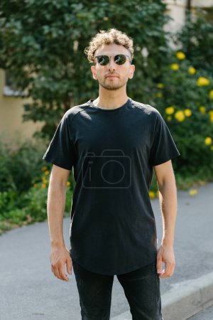 Téléchargez les photos : Hipster beau modèle masculin portant un t-shirt blanc noir avec de l'espace pour votre logo ou design dans un style urbain décontracté - en image libre de droit